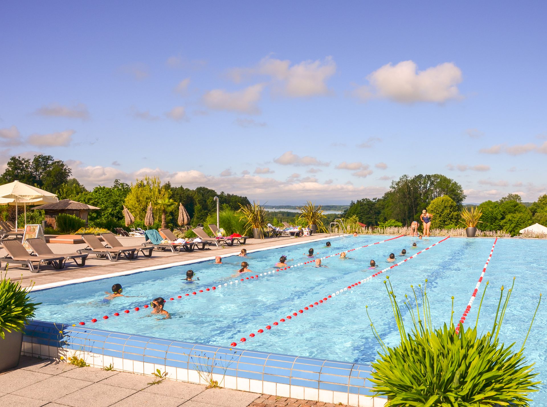 Mehrere Kinder schwimmen im Außenbecken der Chiemgau Thermen während eines Schwimmkurses bei schönem Wetter.