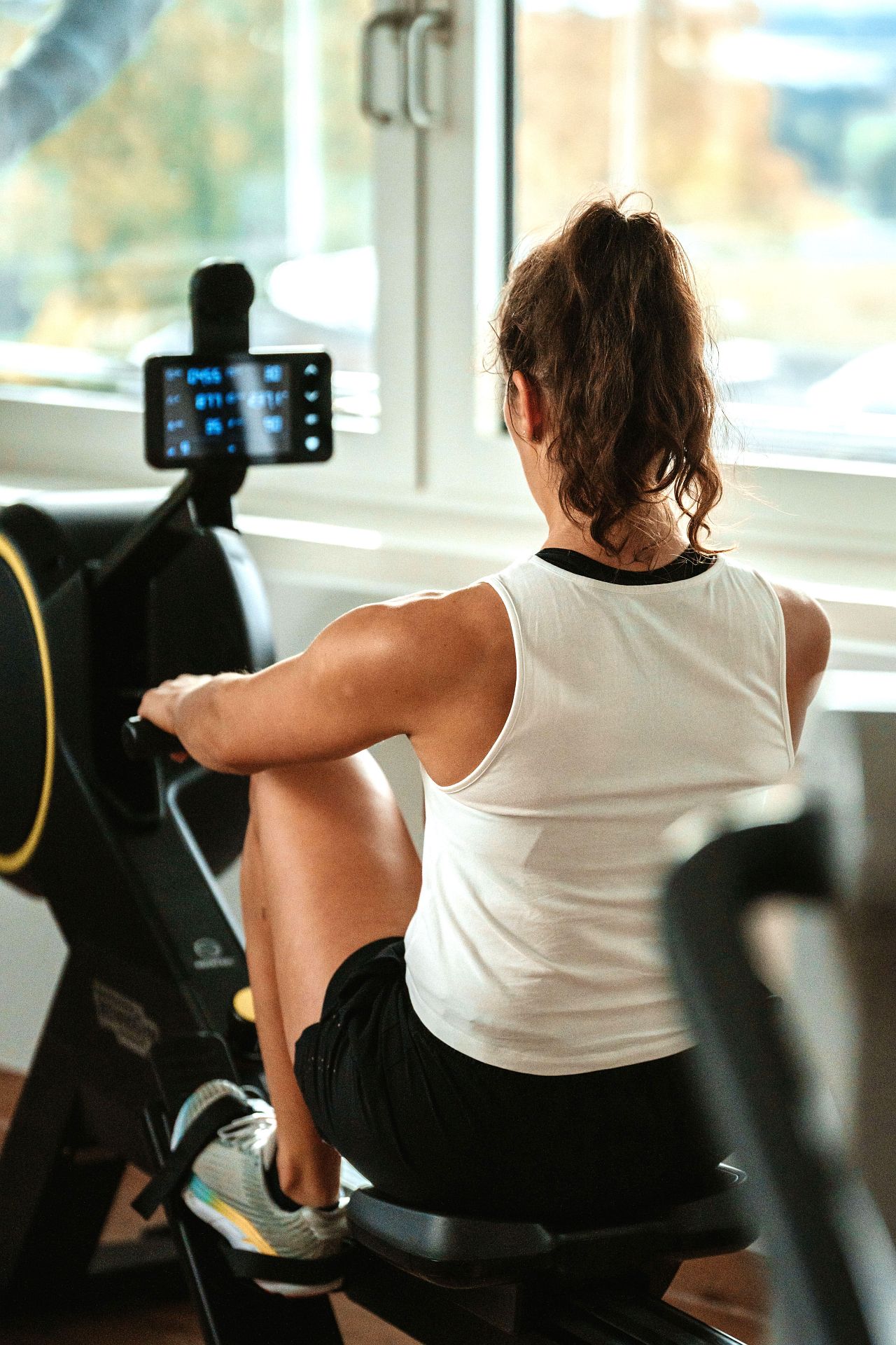 Eine junge Frau trainiert auf dem Rudergerät im PROMOVEO Fitnesszentrum welches von Sonnenschein durchflutet ist.