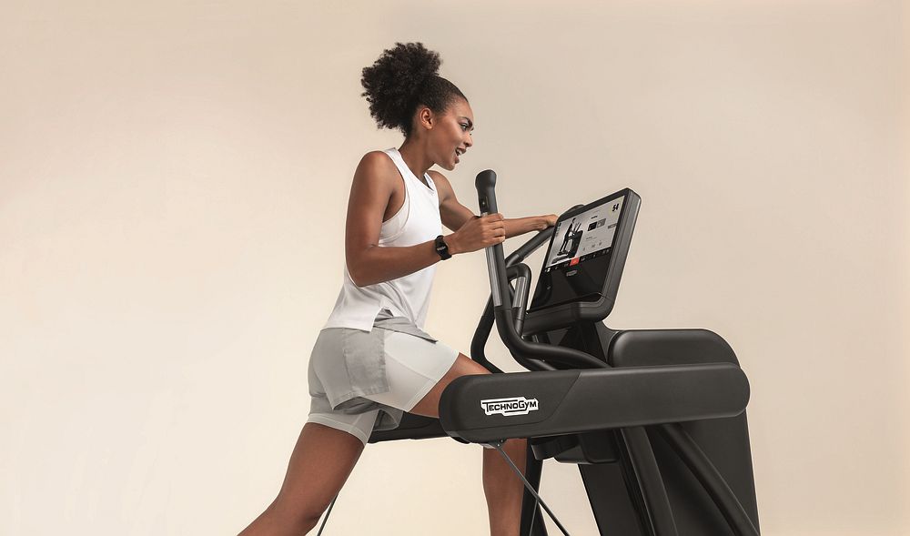 Eine sportliche Frau trainiert dynamisch auf dem Vario-Steppgerät von Technogym.