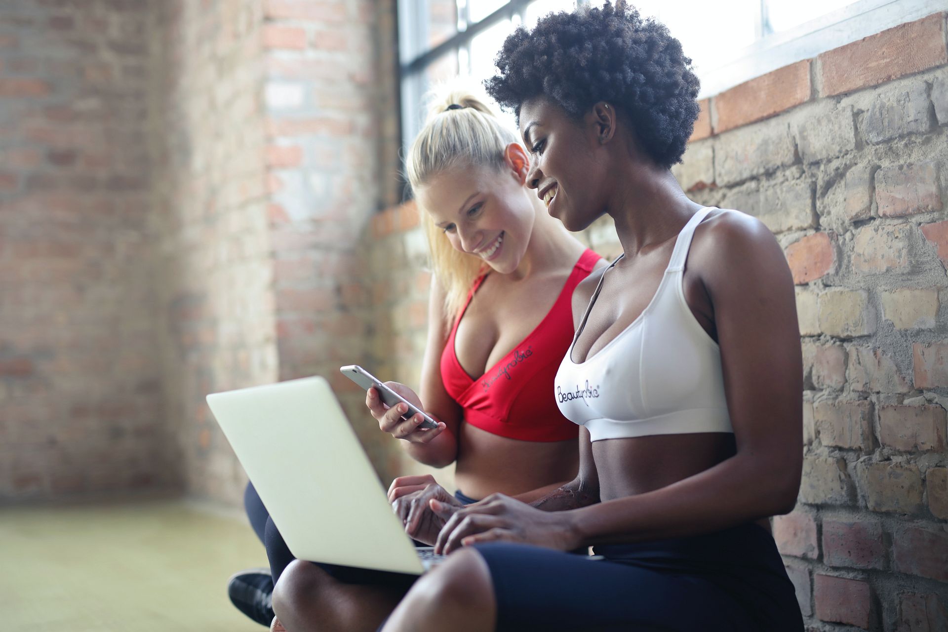 Zwei Frauen Buchen die Kurse direkt am Handy bzw. am Laptop und freuen sich über die einfache Bedienung.
